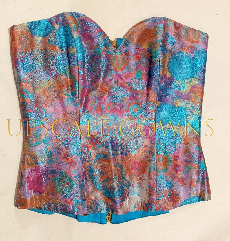 May include: A strapless corset with a vibrant floral print in shades of pink, blue, and orange. The fabric has a metallic sheen and a textured pattern.