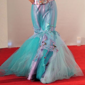 May include: A long, flowing turquoise and lavender tulle skirt with delicate floral embroidery. The skirt is layered and has a mermaid-style silhouette.