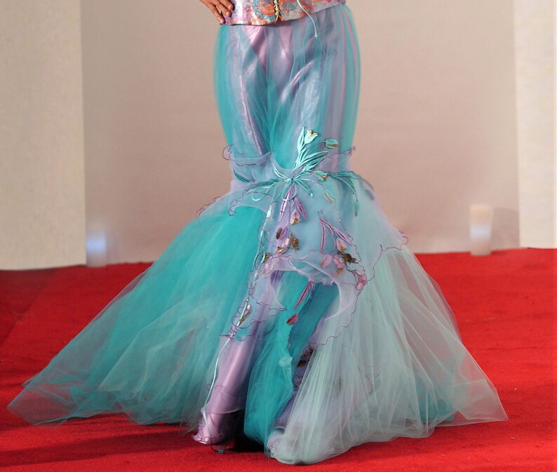 May include: A long, flowing turquoise and lavender tulle skirt with delicate floral embroidery. The skirt is layered and has a mermaid-style silhouette.