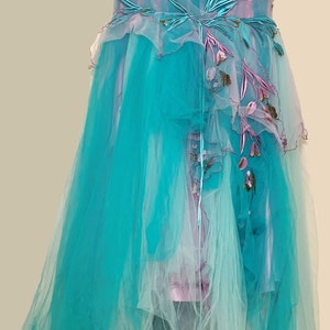 May include: A long, flowing turquoise tulle gown with a pink and white ombre effect. The gown features delicate floral embroidery and a layered skirt.