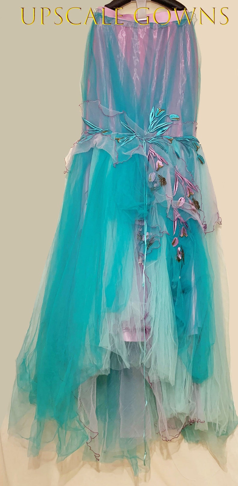 May include: A long, flowing turquoise tulle gown with a pink and white ombre effect. The gown features delicate floral embroidery and a layered skirt.