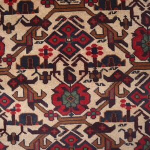 May include: Close-up of a beige rug with a detailed pattern. The design features red, brown, and blue geometric shapes and floral motifs. A blue border with white star-like patterns frames the rug's edge.