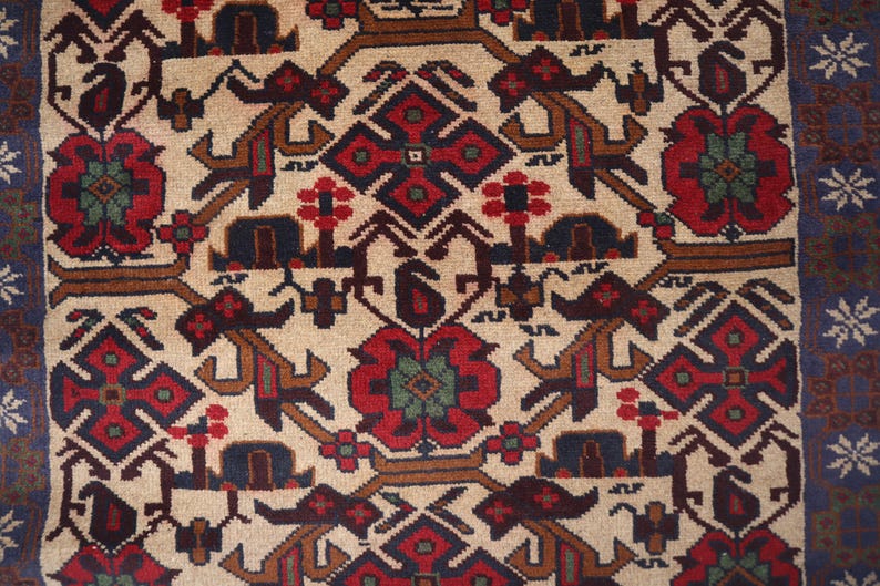 May include: Close-up of a beige rug with a detailed pattern. The design features red, brown, and blue geometric shapes and floral motifs. A blue border with white star-like patterns frames the rug's edge.