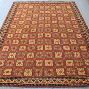 May include: A red, yellow and black patterned rug with a geometric design. The rug has a border with a repeating triangle pattern.