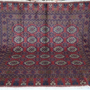 May include: A large rectangular area rug featuring a deep red background with a repeating pattern of dark blue and green geometric medallions. The rug has a wide decorative border with intricate floral motifs and white fringe at the edges.