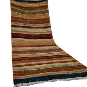 May include: A rectangular rug with horizontal stripes in shades of brown, red, blue, and green. The rug has a fringed edge and a textured appearance, suggesting a woven construction. The colour palette is warm and earthy.