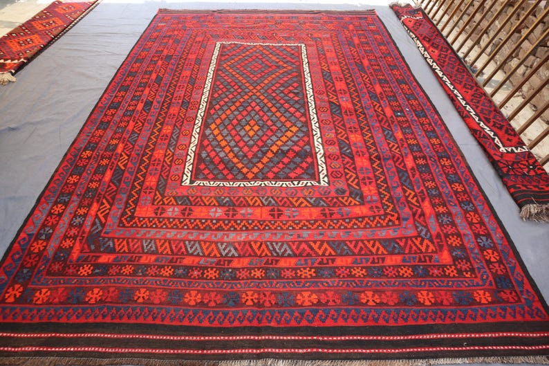 Pu&ograve; includere: Un grande tappeto rettangolare rosso con intricati motivi geometrici nelle tonalit&agrave; del rosso, blu e nero. Il tappeto presenta un disegno centrale a diamante e un bordo bianco. Sono visibili anche due corridori pi&ugrave; piccoli abbinati.