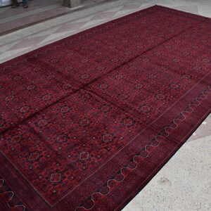 May include: A large, red rug with a detailed, intricate pattern. The rug has a dark blue border with a wavy design.