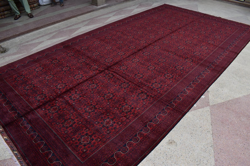 May include: A large, red rug with a detailed, intricate pattern. The rug has a dark blue border with a wavy design.