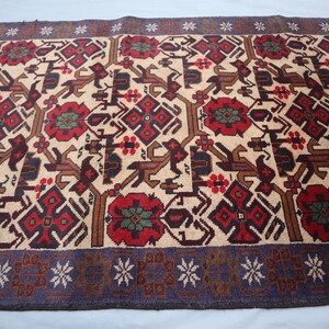 May include: A rectangular rug featuring a beige backdrop with a repeating pattern of red, brown, and dark blue geometric shapes and floral motifs. The rug has a dark blue border with white star-like designs.