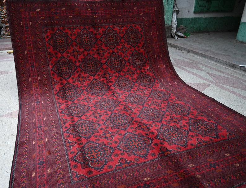 Puede incluir: Una alfombra roja y negra con un dise&ntilde;o floral. La alfombra est&aacute; doblada por la mitad y est&aacute; sobre un suelo de baldosas.