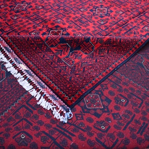 May include: A red and navy blue patterned rug with a geometric design. The rug is folded over, revealing the underside and a white fringe. The rug's pattern includes diamond and floral motifs.