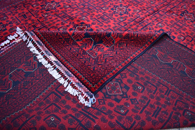 May include: A red and navy blue patterned rug with a geometric design. The rug is folded over, revealing the underside and a white fringe. The rug's pattern includes diamond and floral motifs.