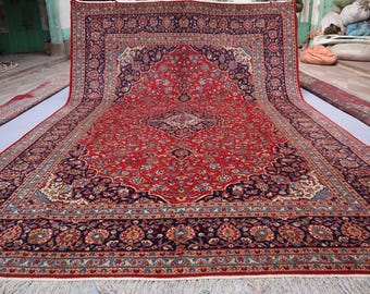 May include: Large, rectangular red rug with an intricate floral pattern and a dark blue border. The rug features a central medallion design and detailed corner motifs. The rug has a fringe along the bottom edge.