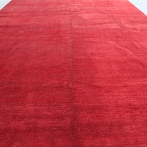 May include: A solid red rug with a subtle sheen. The rug is made of a soft, plush material and has a smooth, even texture.