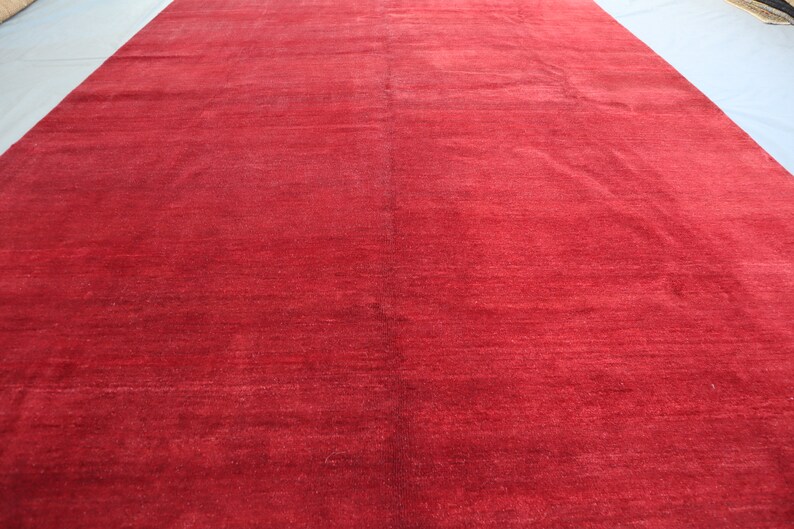 May include: A solid red rug with a subtle sheen. The rug is made of a soft, plush material and has a smooth, even texture.