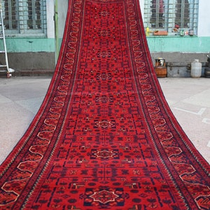 Könnte beinhalten: Ein langer, roter Läufer mit traditionellem persischem Design. Der Teppich hat einen dunkelblauen Rand mit komplizierten Mustern und eine rote Mitte mit einem sich wiederholenden geometrischen Muster.