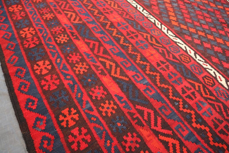 Pu&ograve; includere: Un vivace tappeto tessuto a mano con un ricco arazzo di colori. Il design presenta audaci motivi geometrici rossi, blu scuro e marroni. I dettagli intricati e i toni caldi del tappeto creano un tessuto visivamente accattivante.