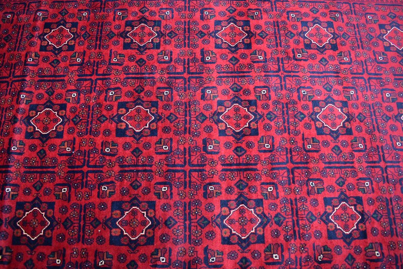 May include: A red rug with a repeating pattern of blue and white geometric shapes. The rug has a traditional Persian design.