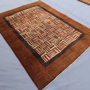 Könnte beinhalten: Rechteckiger brauner Teppich mit einem gewebten Muster in Braun-, Beige- und Rottönen. Der Teppich hat einen dunkelbraunen Rand und einen hellbraunen äußeren Rand. Das Design zeigt ein sich wiederholendes geometrisches Muster.