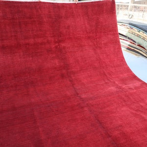 May include: A solid red rug with a smooth, slightly textured surface. The rug is folded in half and laid out on a white surface.