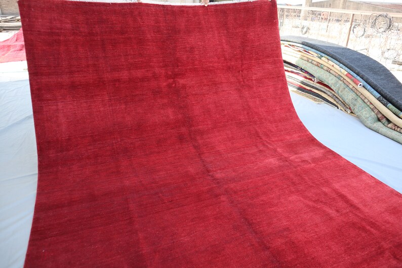 May include: A solid red rug with a smooth, slightly textured surface. The rug is folded in half and laid out on a white surface.