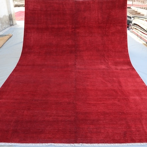 May include: A solid red rug with a white fringe border. The rug is laid out flat on a white surface.