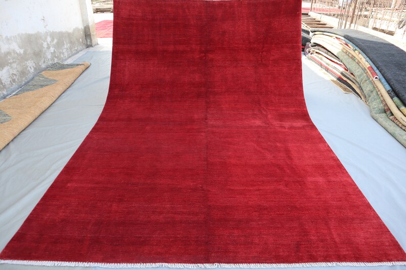 May include: A solid red rug with a white fringe border. The rug is laid out flat on a white surface.