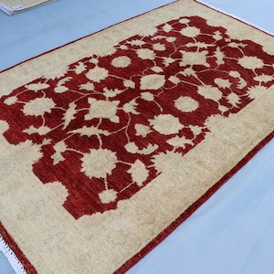 May include: A beige and red rug with a floral pattern. The rug has a white fringe border.