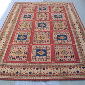 May include: A red, beige and blue patterned rug with a geometric design. The rug has a border with a repeating pattern of stylised leaves.