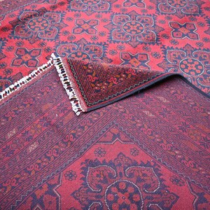 Puede incluir: Una alfombra roja y negra con estampado y borde de flecos. La alfombra est&aacute; doblada por la mitad, mostrando el intrincado dise&ntilde;o en ambos lados.