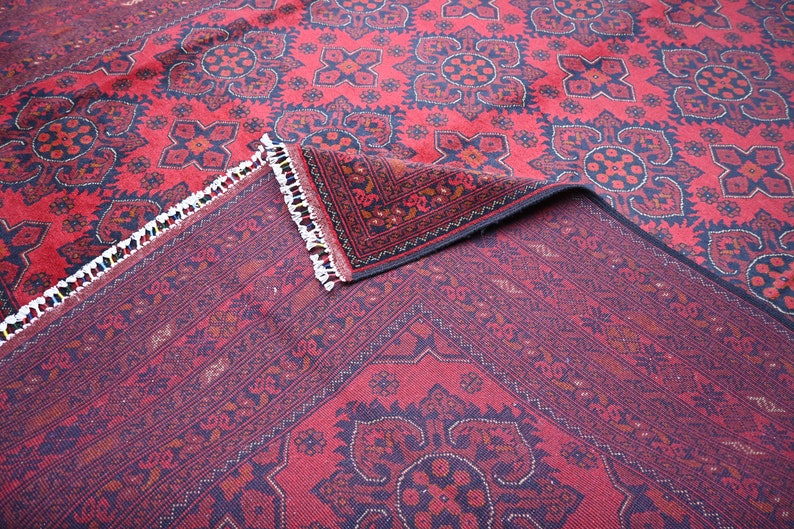 Puede incluir: Una alfombra roja y negra con estampado y borde de flecos. La alfombra est&aacute; doblada por la mitad, mostrando el intrincado dise&ntilde;o en ambos lados.