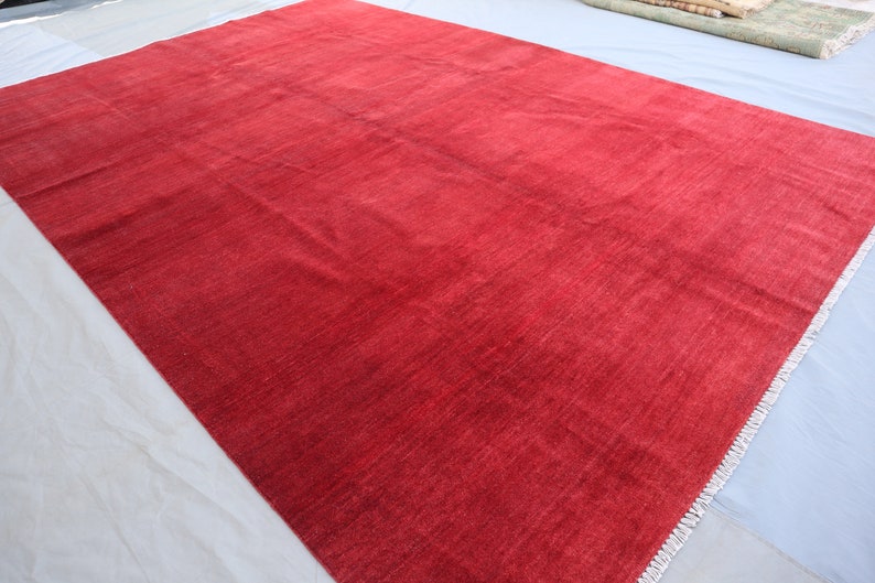 May include: A solid red rug with a subtle texture and a fringed edge.