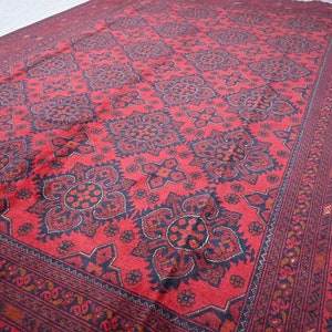 Puede incluir: Una alfombra roja con un patr&oacute;n geom&eacute;trico en blanco y negro. La alfombra tiene un borde con un patr&oacute;n repetitivo de peque&ntilde;as flores.