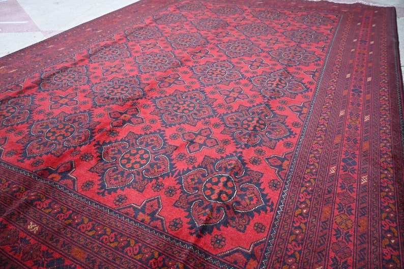 Puede incluir: Una alfombra roja con un patr&oacute;n geom&eacute;trico en blanco y negro. La alfombra tiene un borde con un patr&oacute;n repetitivo de peque&ntilde;as flores.
