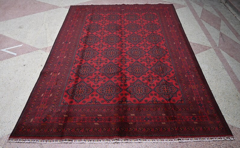 Puede incluir: Una alfombra roja con un dise&ntilde;o estampado en azul oscuro y rojo. La alfombra tiene un borde con flecos.