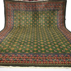 May include: A large, rectangular green rug with an intricate pattern of repeating floral and geometric designs. The rug features a dark border with red and blue accents, and a central field of green with yellow and red floral motifs.
