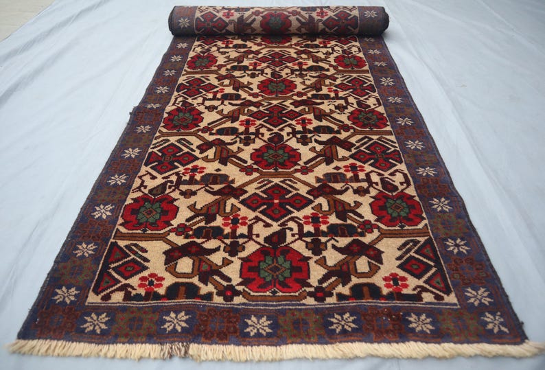 May include: Rolled-up beige runner rug with a detailed pattern. The design features red, brown, and green floral and geometric shapes. The border is dark blue with white star-like patterns and a cream fringe.