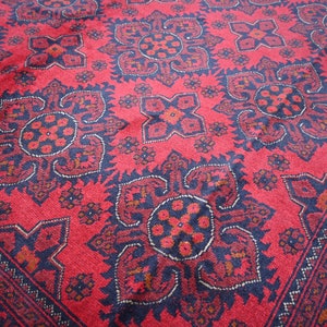Puede incluir: Una alfombra roja con un dise&ntilde;o persa tradicional que presenta intrincados patrones florales en blanco y negro. La alfombra tiene un borde azul oscuro con un patr&oacute;n geom&eacute;trico.