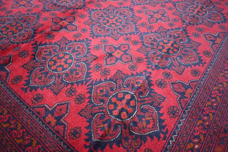Puede incluir: Una alfombra roja con un dise&ntilde;o persa tradicional que presenta intrincados patrones florales en blanco y negro. La alfombra tiene un borde azul oscuro con un patr&oacute;n geom&eacute;trico.