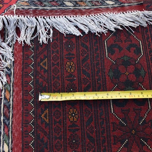 Może przedstawiać: Zbliżenie na czerwony, czarno-biały dywan z frędzlami. Na dywanie leży ż&oacute;łta miara taśmowa, pokazująca pomiar 33 cm.