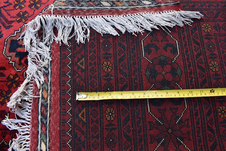 Może przedstawiać: Zbliżenie na czerwony, czarno-biały dywan z frędzlami. Na dywanie leży ż&oacute;łta miara taśmowa, pokazująca pomiar 33 cm.