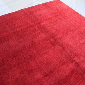 May include: A solid red rug with a smooth, slightly textured surface. The rug is made of a soft, plush material.