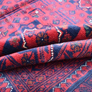 May include: A red and blue patterned rug with a traditional design. The rug is folded in half, showing the intricate details of the weave.