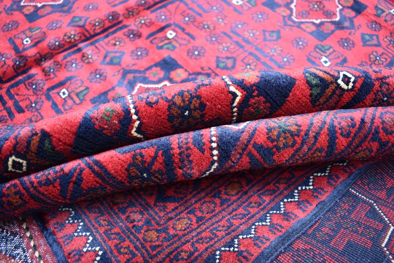 May include: A red and blue patterned rug with a traditional design. The rug is folded in half, showing the intricate details of the weave.