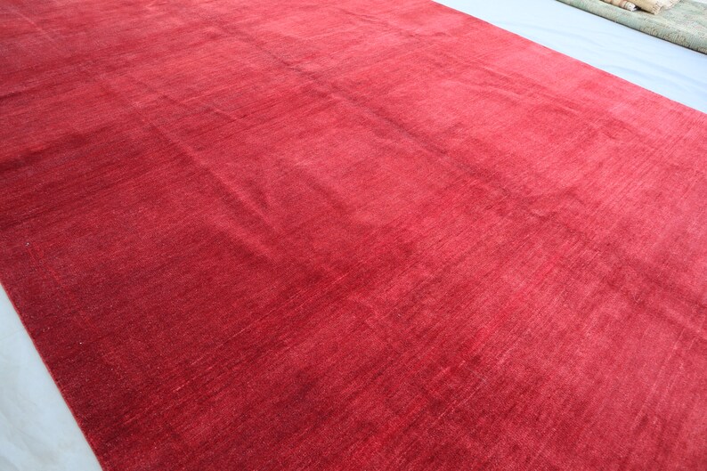 May include: A solid red rug with a smooth, slightly textured surface. The rug is made of a soft, plush material.