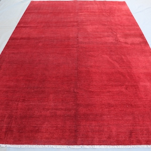 May include: A solid red rug with a subtle sheen. The rug has a simple design and a fringed edge.