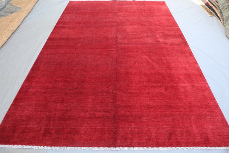 May include: A solid red rug with a subtle sheen. The rug has a simple design and a fringed edge.