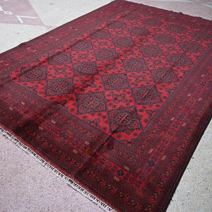 Puede incluir: Una alfombra roja con un dise&ntilde;o persa tradicional. La alfombra tiene un fondo rojo oscuro con intrincados patrones negros y dorados. La alfombra tiene un borde con flecos.
