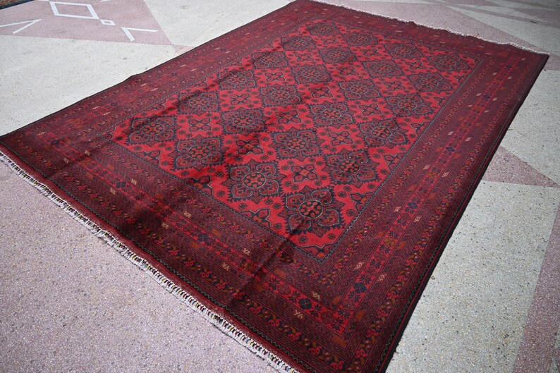 Puede incluir: Una alfombra roja con un dise&ntilde;o persa tradicional. La alfombra tiene un fondo rojo oscuro con intrincados patrones negros y dorados. La alfombra tiene un borde con flecos.